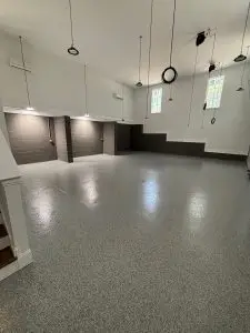 Spacious garage with polished epoxy flooring, multiple hanging pendant lights, gray accent walls, and high windows providing natural light.